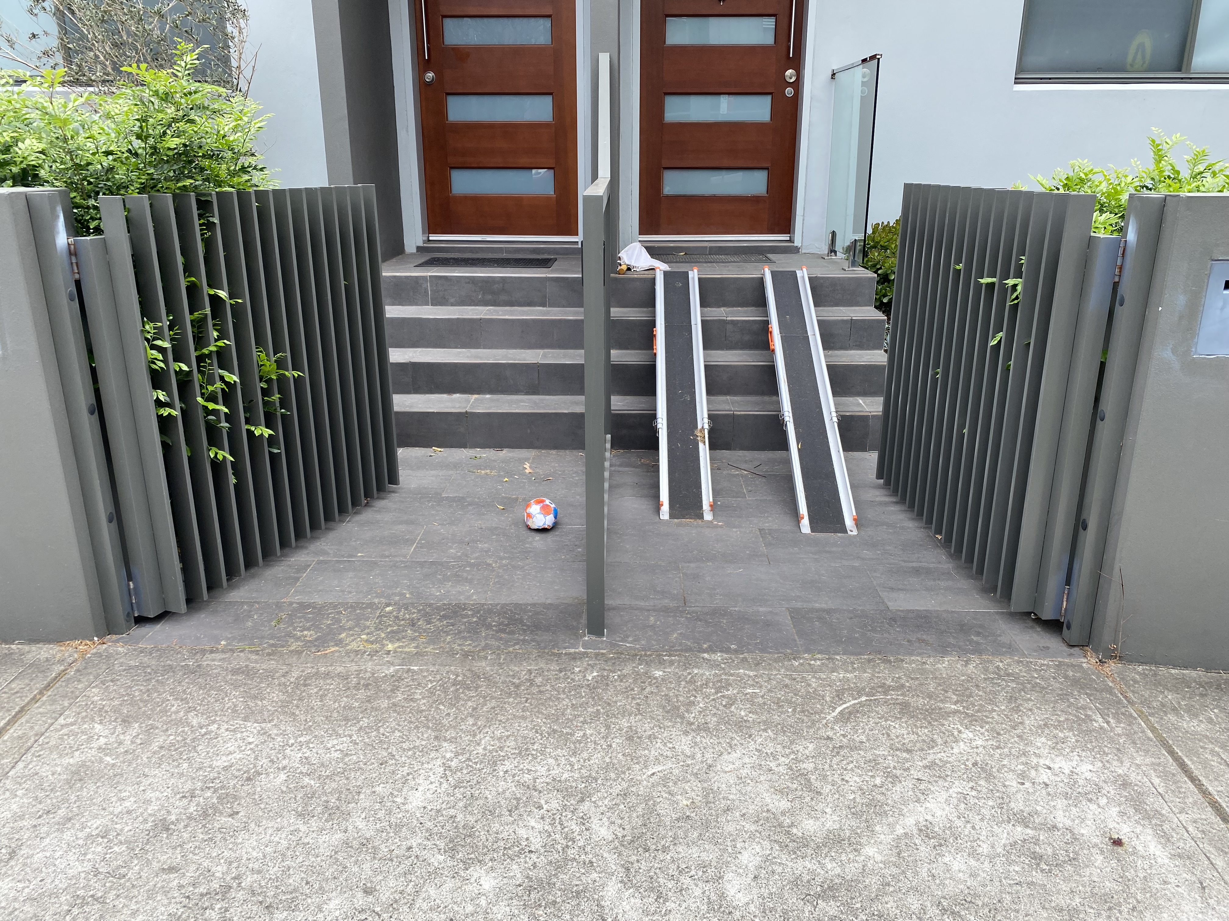 Two terrace front doors next to each other, behind low front gates. One of the stairs has a pair of ramps fitted to it.